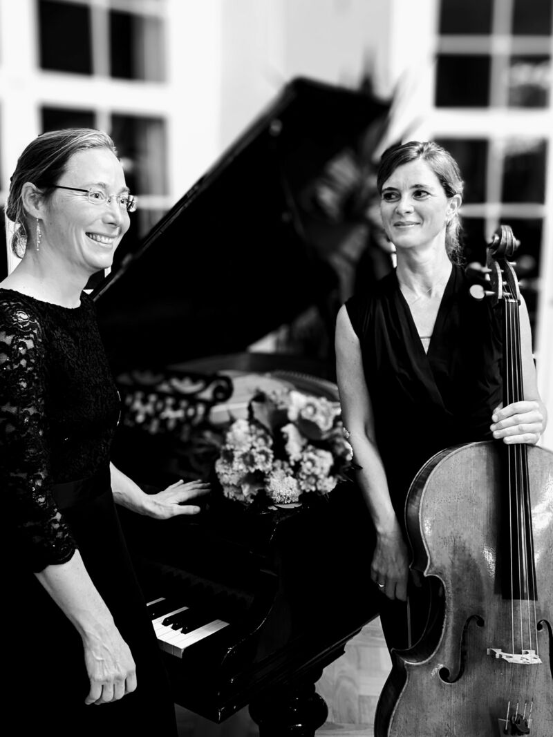 Das Schwarzweiß-Foto zeigt die Solocellistin der Hamburger Philharmonie Olivia Jeremias mit Pianistin Kerstin Loeper am aufgeklapten Flügel stehend
